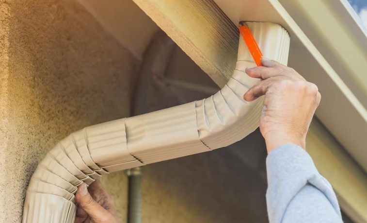 Installer fitting a new downspout section to a home